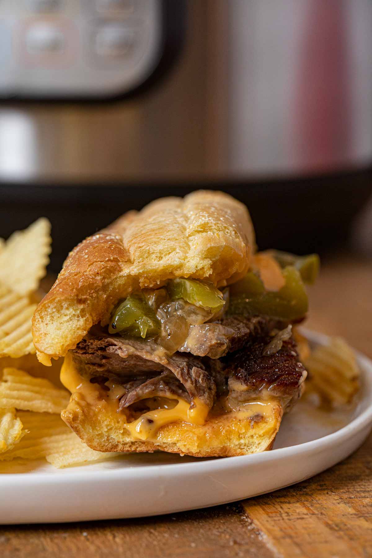 Instant Pot Philly Cheese Steak Sandwich partially eaten on plate with chips