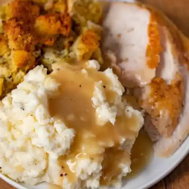 gravy on top of mashed potatoes with turkey and stuffing on a plate