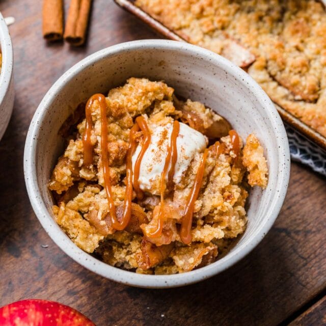 Sheet Pan Apple Crisp served in a white bowl with vanilla ice cream and caramel.