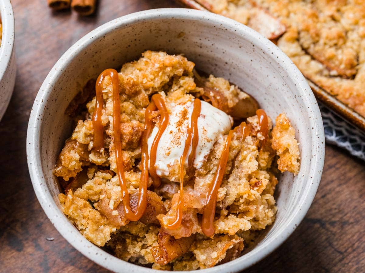 Sheet Pan Apple Crisp served in a white bowl topped with whipped cream.