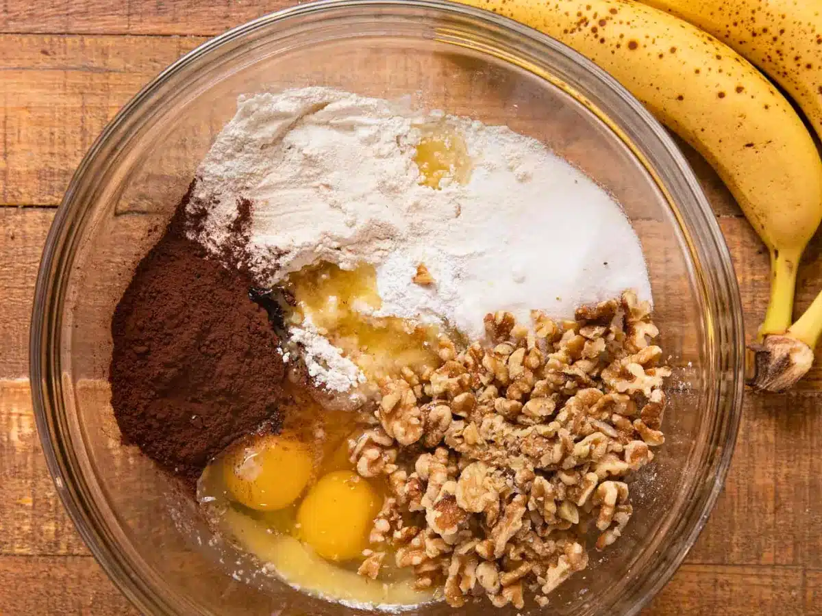 eggs, flour, banana, powder, and nuts in a glass bowl