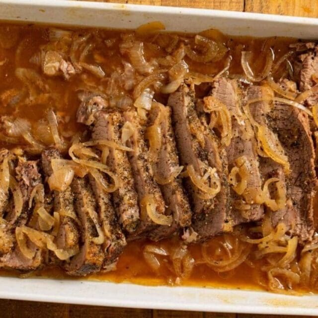 Sliced brisket with onion in a white baking pan.