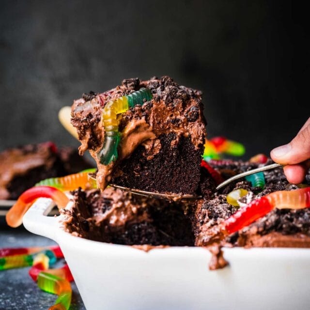Chocolate Pudding Dirt Cake with pudding, crushed oreos, and gummy worms on top in baking dish with slice lifting