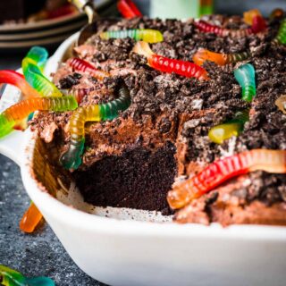 Chocolate Pudding Dirt Cake with pudding, crushed oreos, and gummy worms on top in baking dish with slice missing