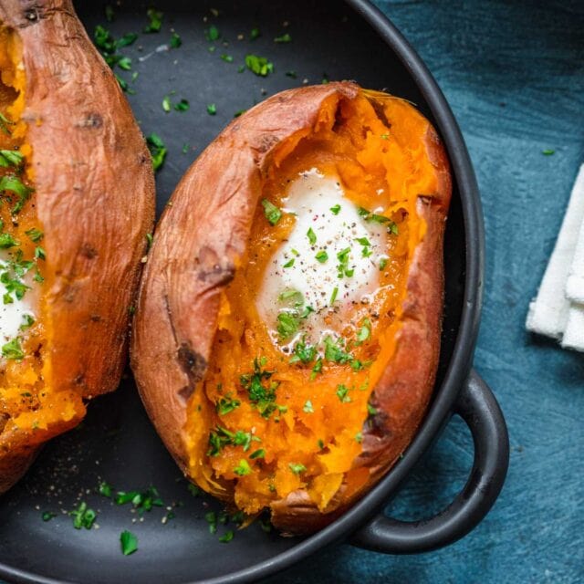 cooked sweet potatoes in bowl, cut open with butter and parsley garnish