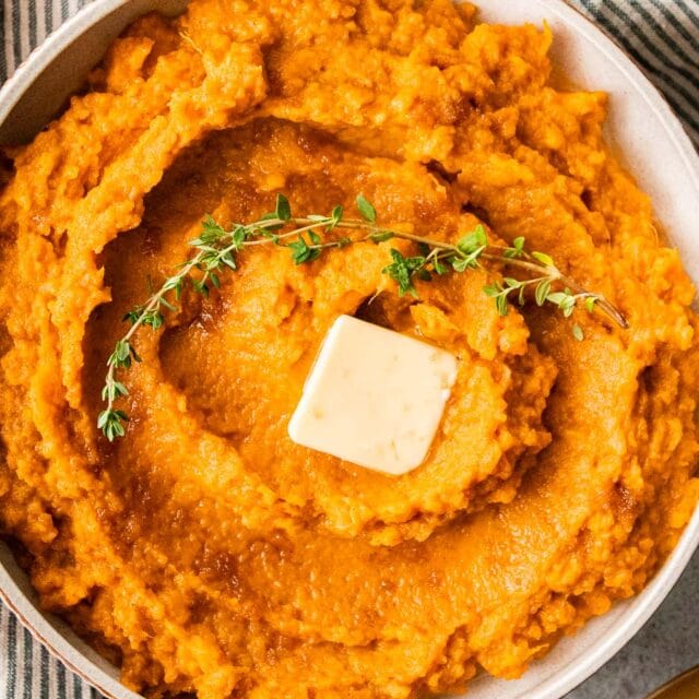 Creamy mashed sweet potatoes with pat of butter and garnish.