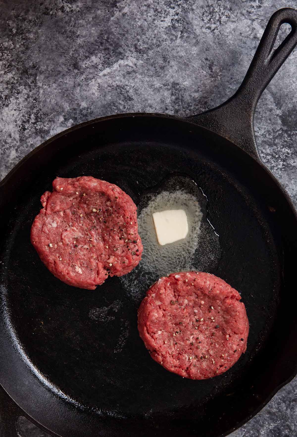 Stovetop Burgers raw patties in cast iron skillet with melted butter