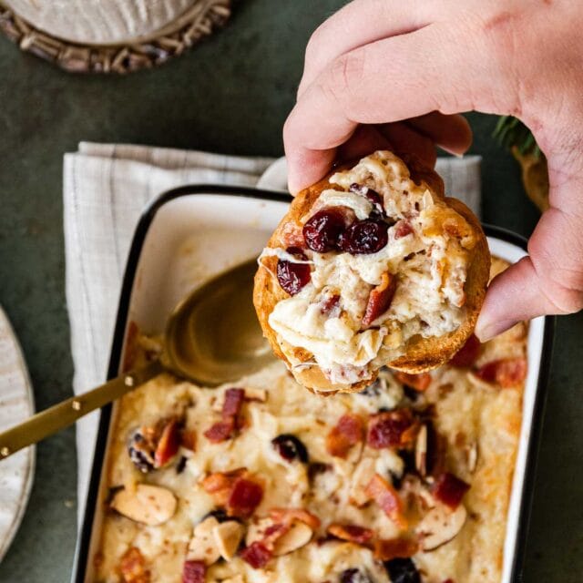 Bacon Cranberry Swiss Cheese Dip in baking dish with spoon and french bread slice