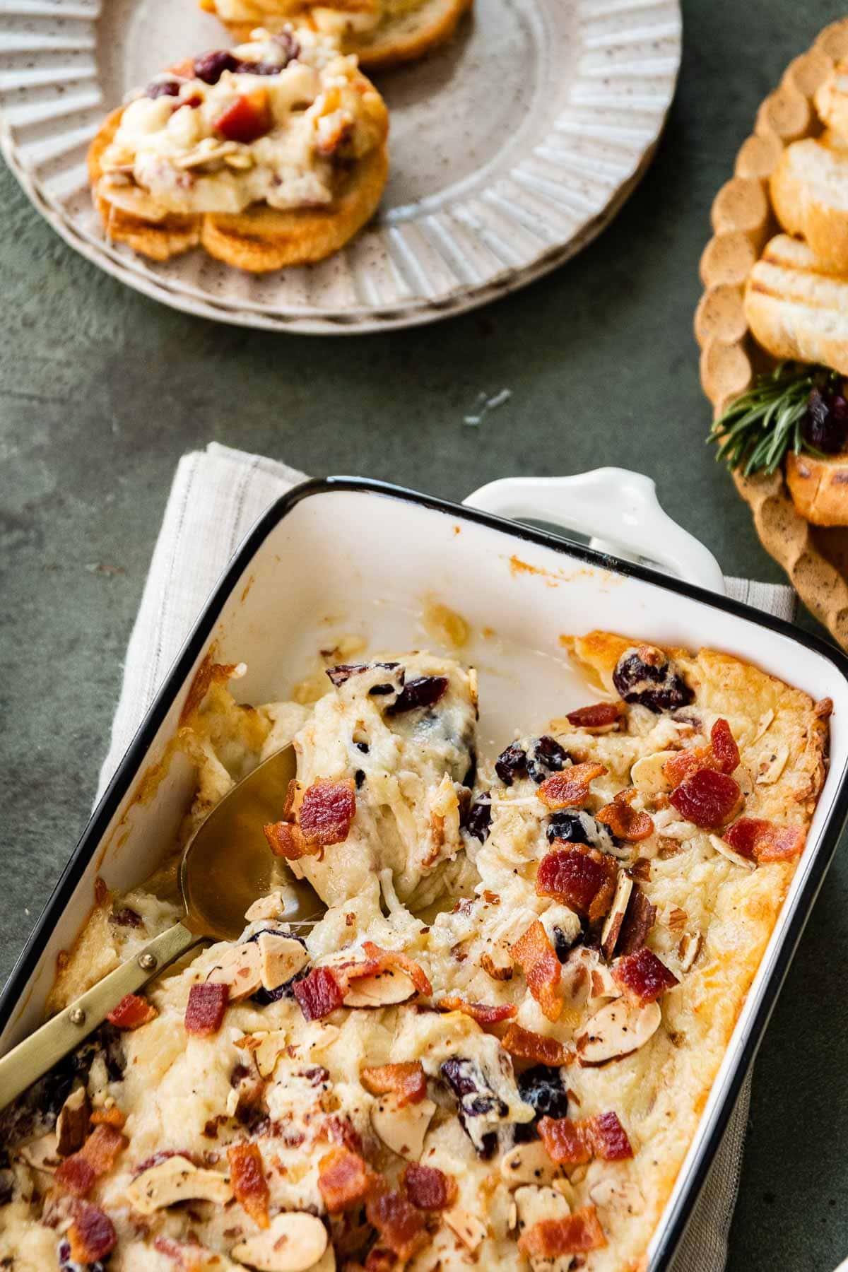 Bacon Cranberry Swiss Cheese Dip in baking dish with spoon and french bread slices