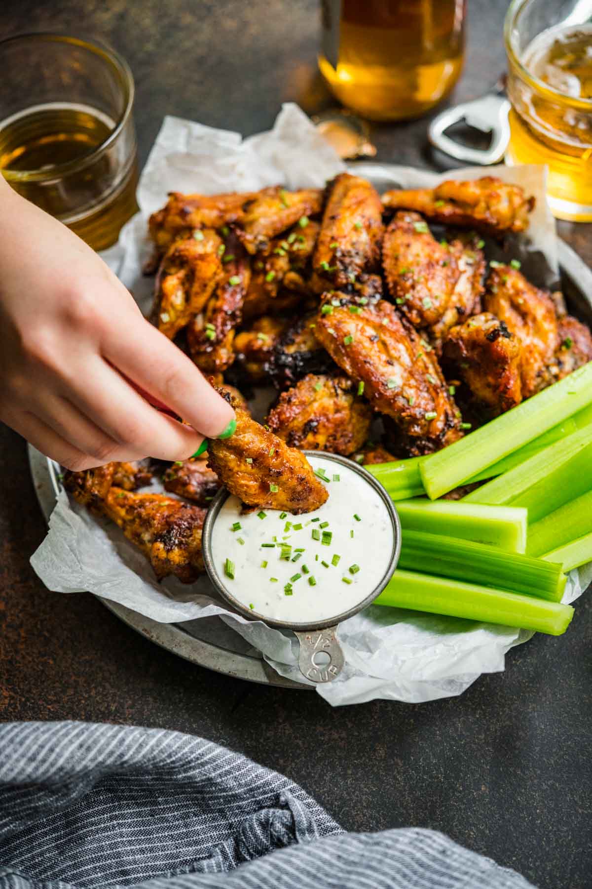 Baked Chicken Wings on serving plate with celery and hand dipping wing in creamy dip