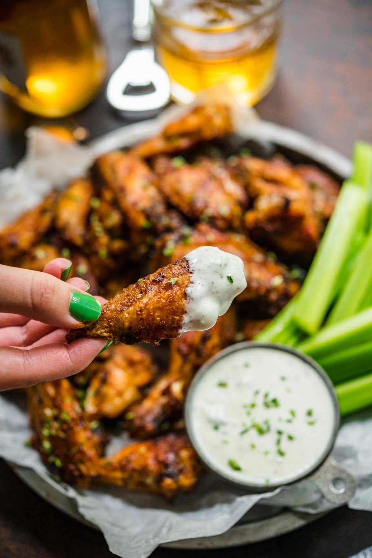 Baked Chicken Wings on serving plate with celery and hand dipping wing in creamy dip