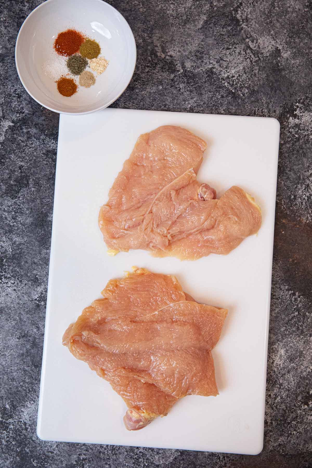 Blackened Chicken raw chicken breast on cutting board with rub ingredients in bowl