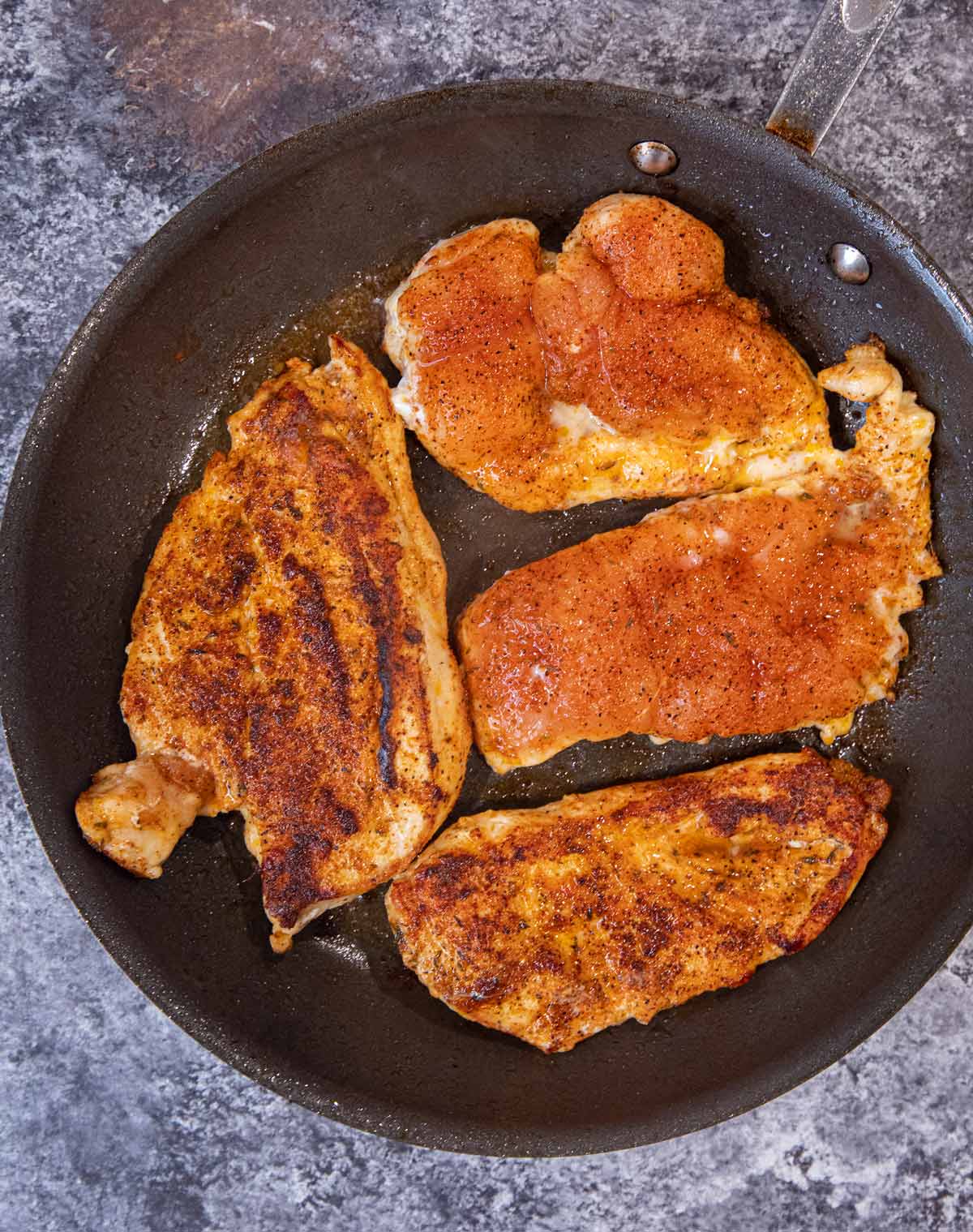 Blackened Chicken in frying pan, with two pieces cooked on top and two pieces uncooked on top