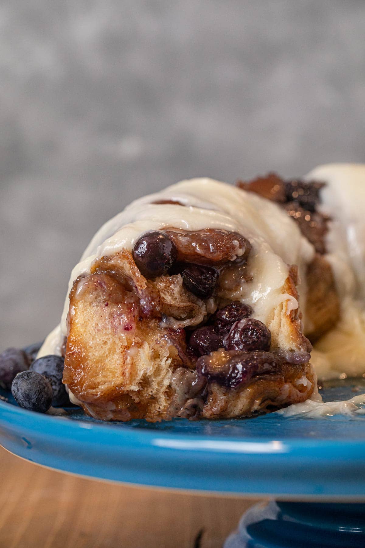 Blueberry Cream Cheese Monkey Bread with pieces removed on cake stand with icing