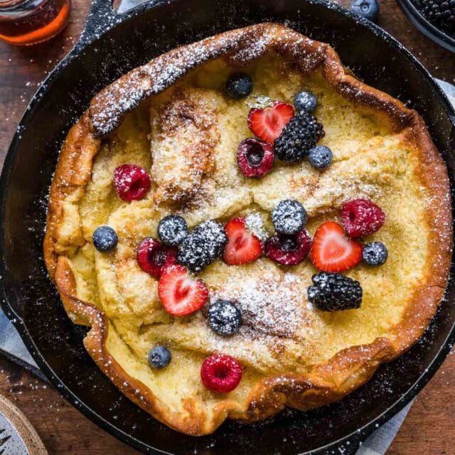 Skillet Baked Pancake in cast iron skillet with fresh berries and maple syrup