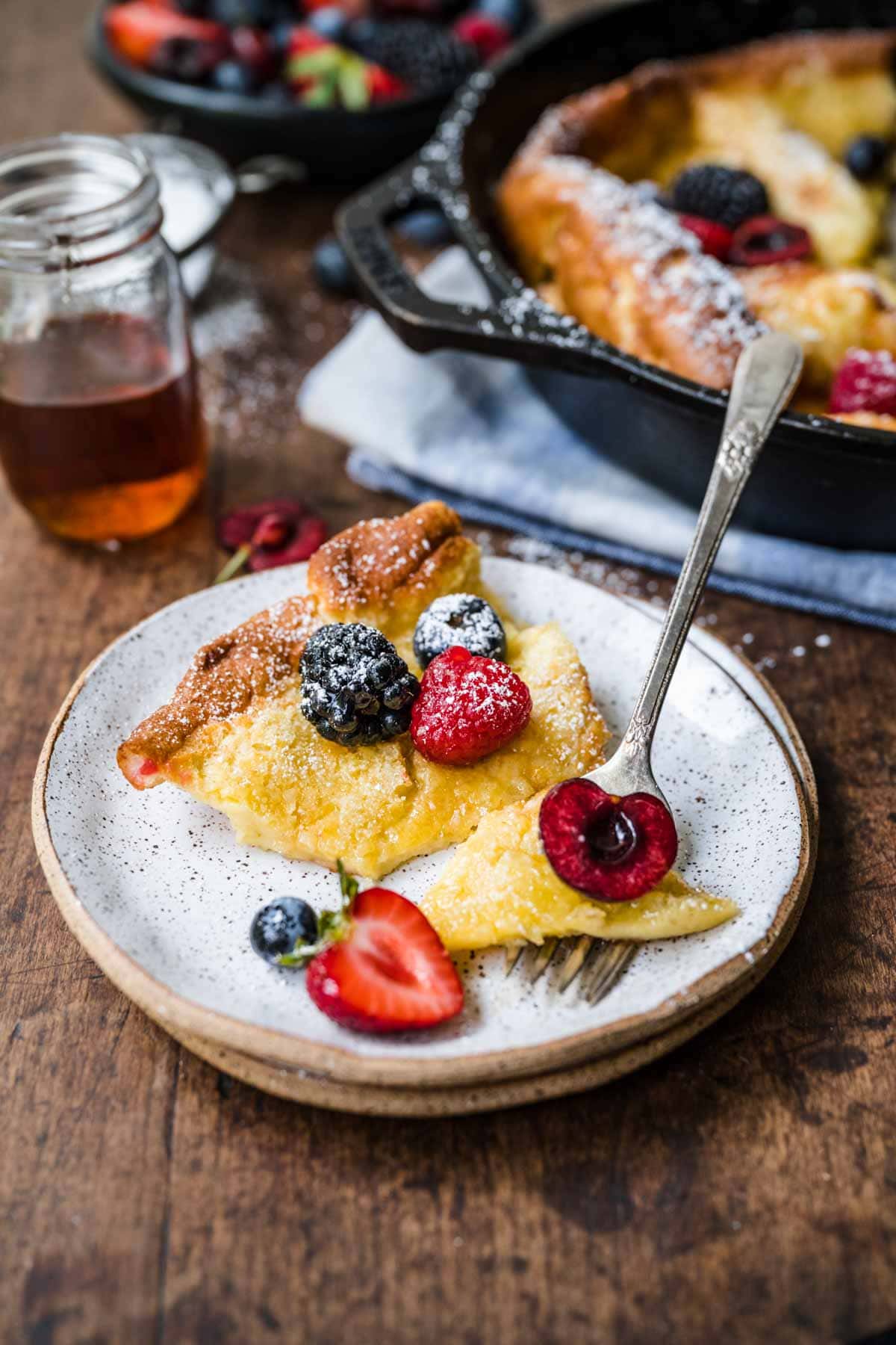 Skillet Baked Pancake slice on plate with fresh berries and maple syrup