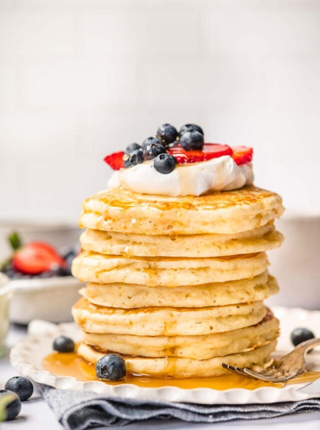 Perfect Fluffy Pancakes stacked on a plate with whipped cream, fresh berries, and maple syrup