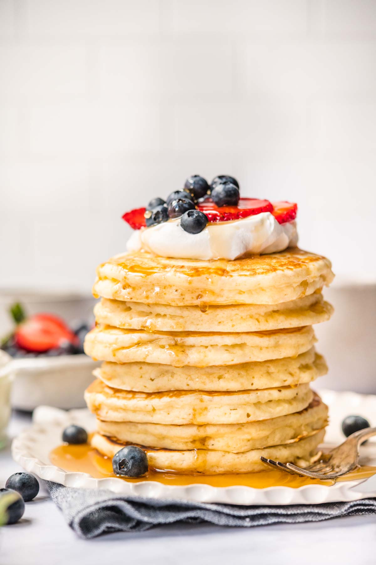 Perfect Fluffy Pancakes stacked on a plate with whipped cream, fresh berries, and maple syrup