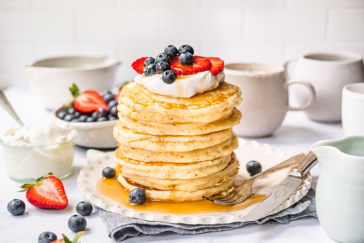 Perfect Fluffy Pancakes stacked on a plate with whipped cream, fresh berries, and maple syrup