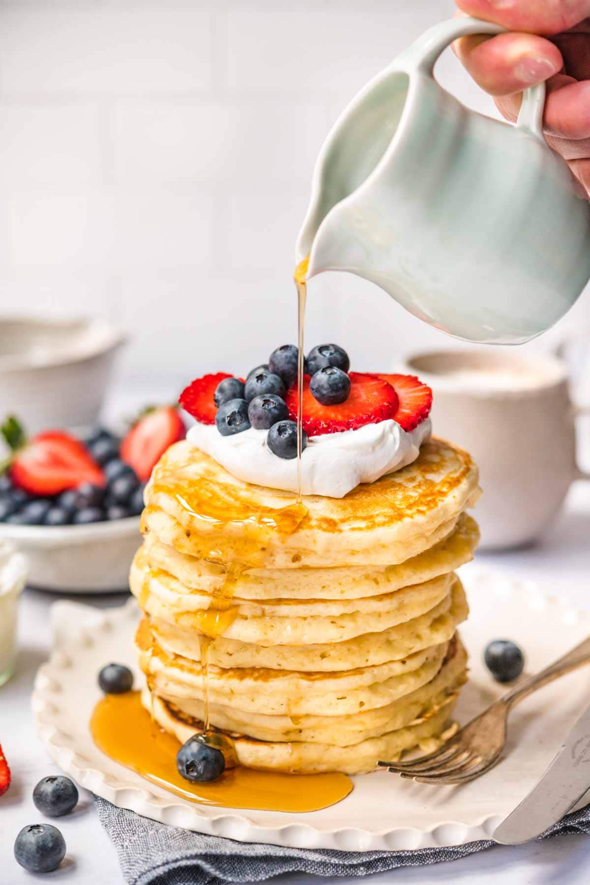 Perfect Fluffy Pancakes stacked on a plate with whipped cream, fresh berries, and maple syrup