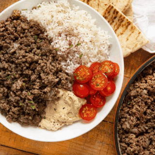 beef, rice, tomatoes, and hummus in a bowl with pita bread on the side