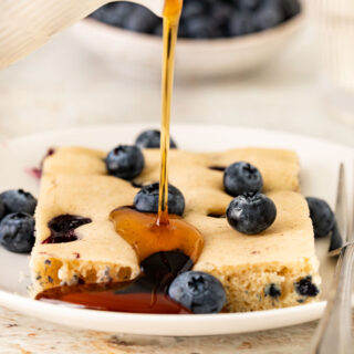 Sheet Pan Blueberry Pancakes slice on plate with maple syrup drizzled