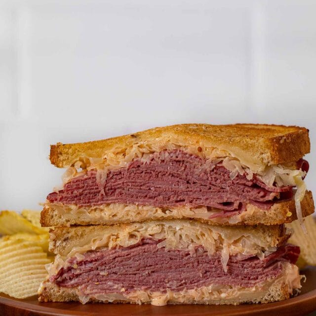 Reuben Sandwich halves in stack on plate with chips