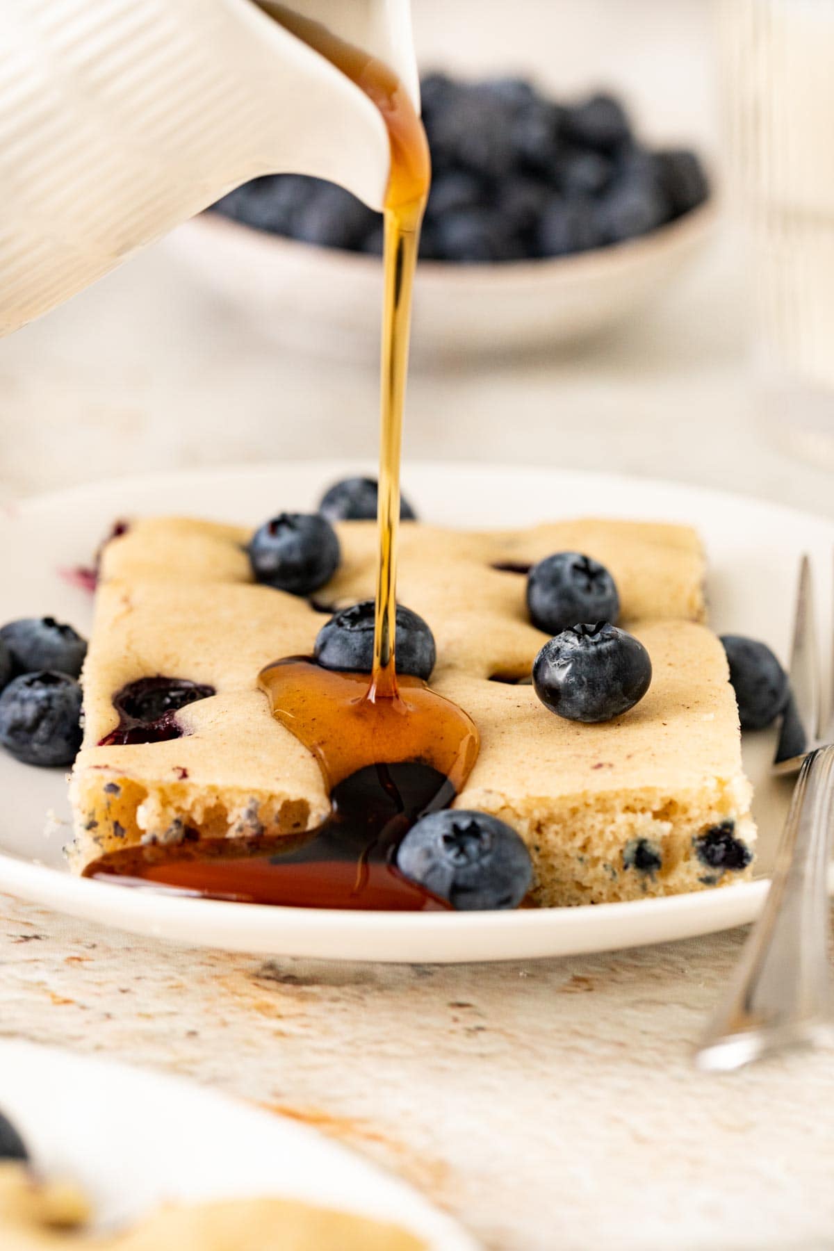 Sheet Pan Blueberry Pancakes slice on plate with maple syrup drizzled