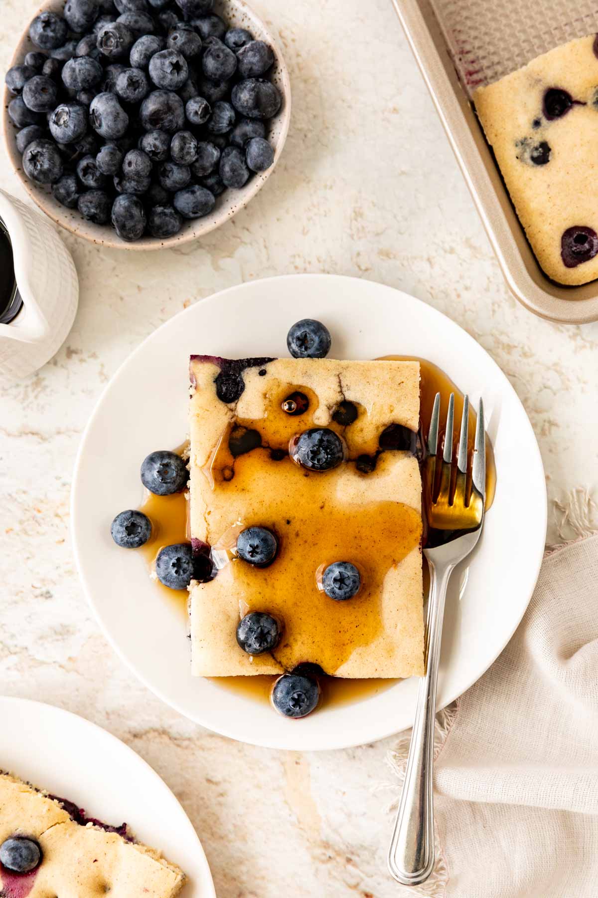 Sheet Pan Blueberry Pancakes slice on plate with maple syrup and fresh blueberry garnish