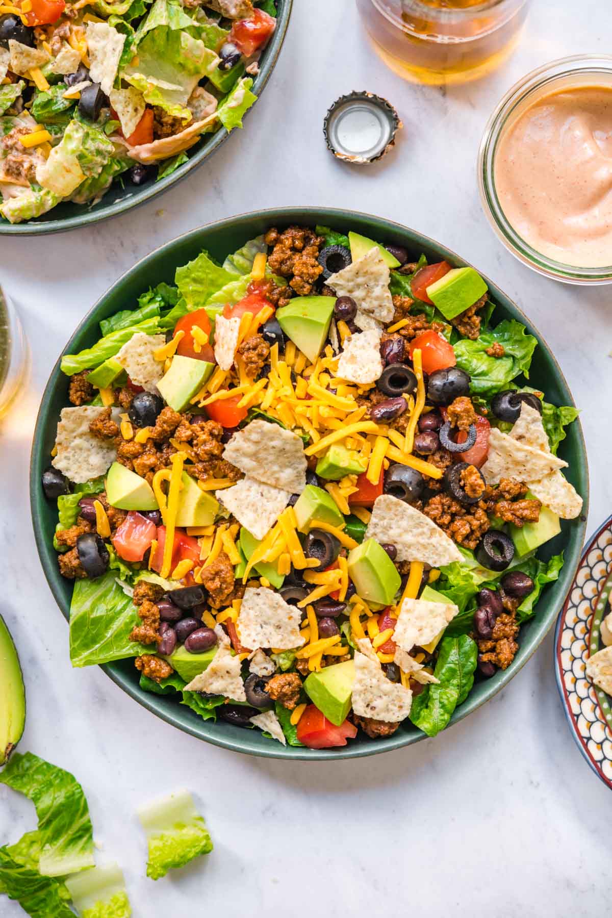 Assembled Taco Salad in bowl with lettuce, black beans, seasoned ground beef, shredded cheese, avocado.