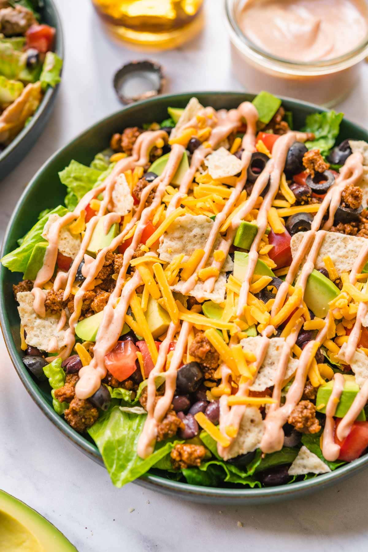 Assembled Taco Salad in bowl with lettuce, black beans, seasoned ground beef, shredded cheese, avocado, and dressing.