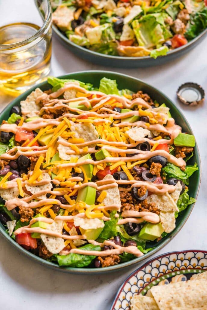 Assembled Taco Salad in bowl with lettuce, black beans, seasoned ground beef, shredded cheese, avocado, and dressing.