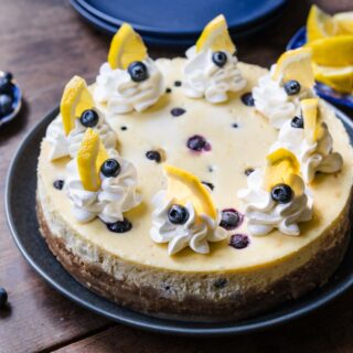 Blueberry Lemon Cheesecake on serving plate with whipped cream, fresh blueberries and lemon garnish