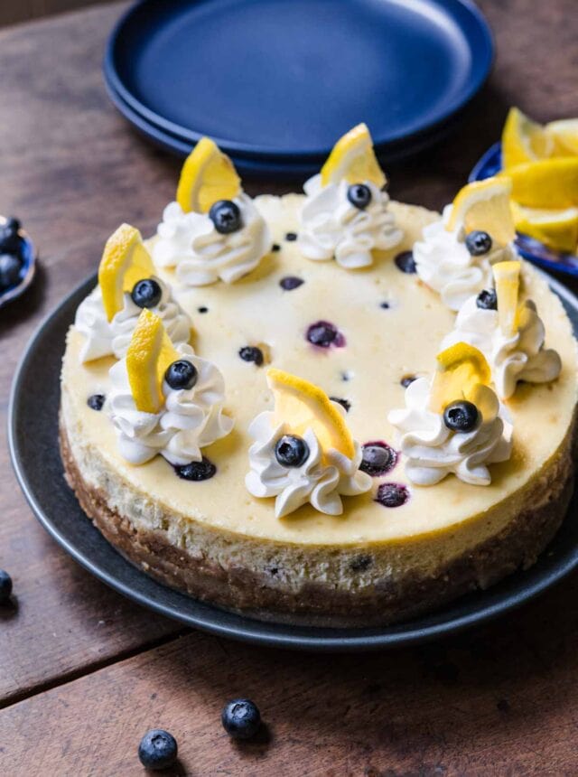 Blueberry Lemon Cheesecake on serving plate with whipped cream, fresh blueberries and lemon garnish