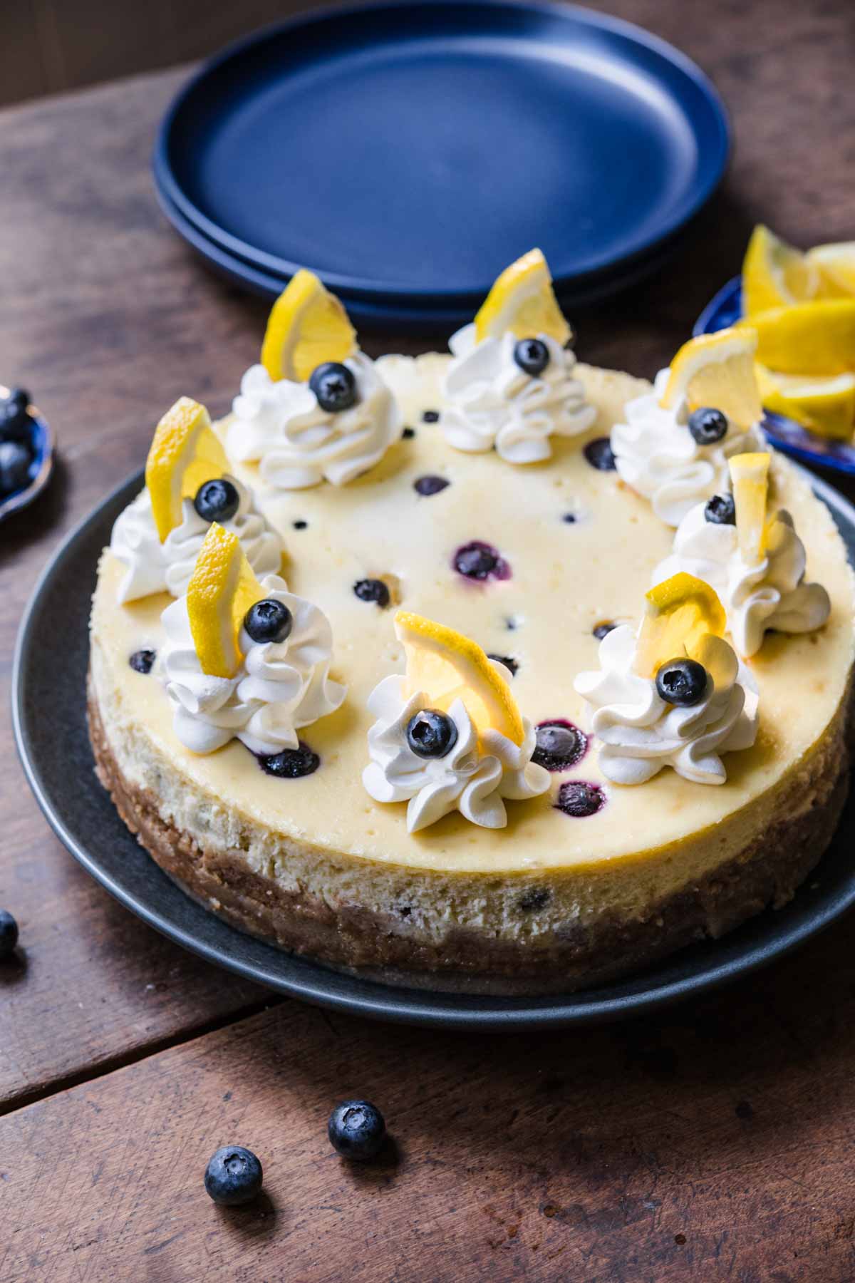 Blueberry Lemon Cheesecake on serving plate with whipped cream, fresh blueberries and lemon garnish