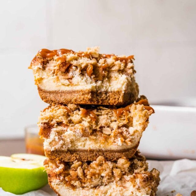 Caramel Apple Crumb Cheesecake Bars sliced on parchment with caramel sauce drizzled on top