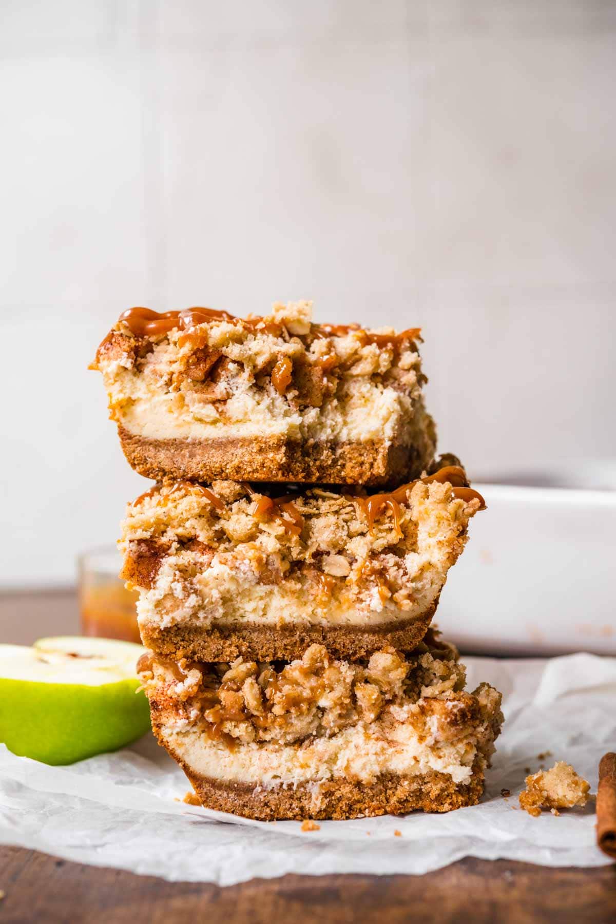 Caramel Apple Crumb Cheesecake Bars sliced on parchment with caramel sauce drizzled on top