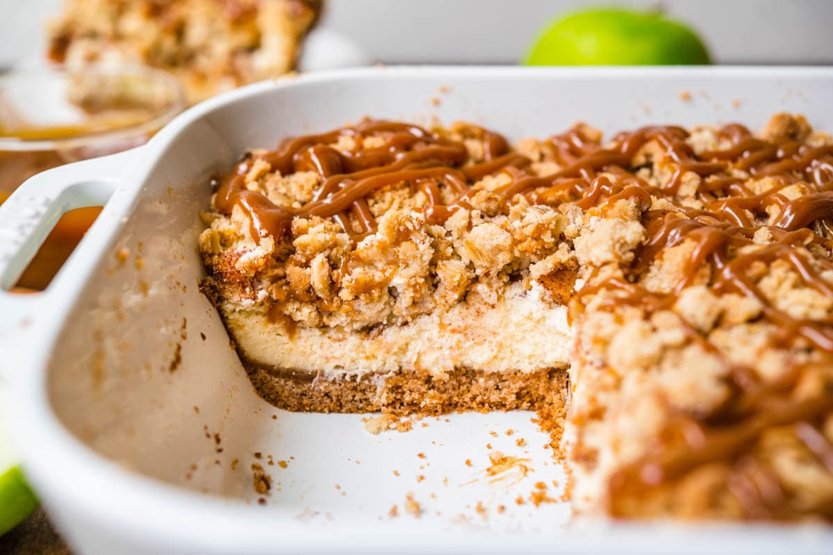 Caramel Apple Crumb Cheesecake Bars sliced in baking dish with caramel sauce drizzled on top