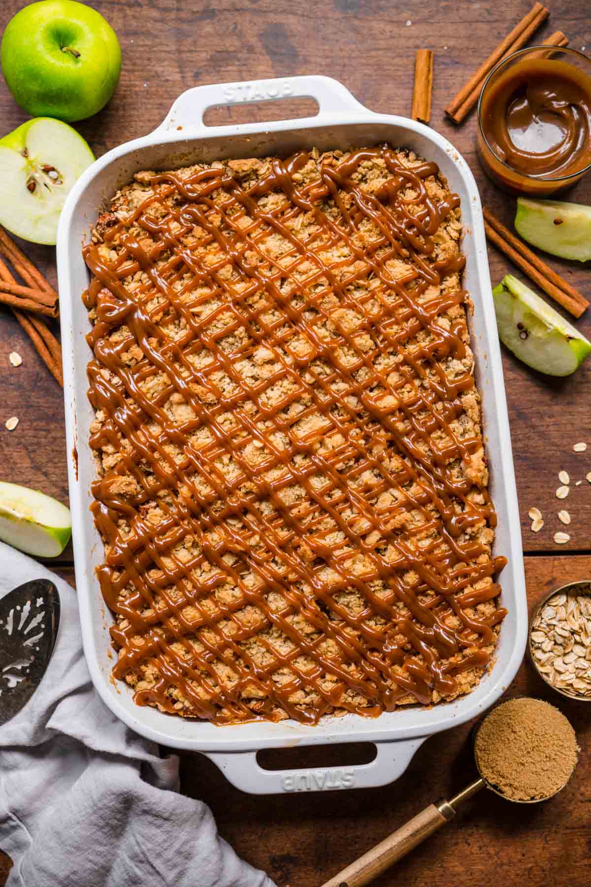 Caramel Apple Crumb Cheesecake Bars in baking dish with caramel sauce drizzled on top