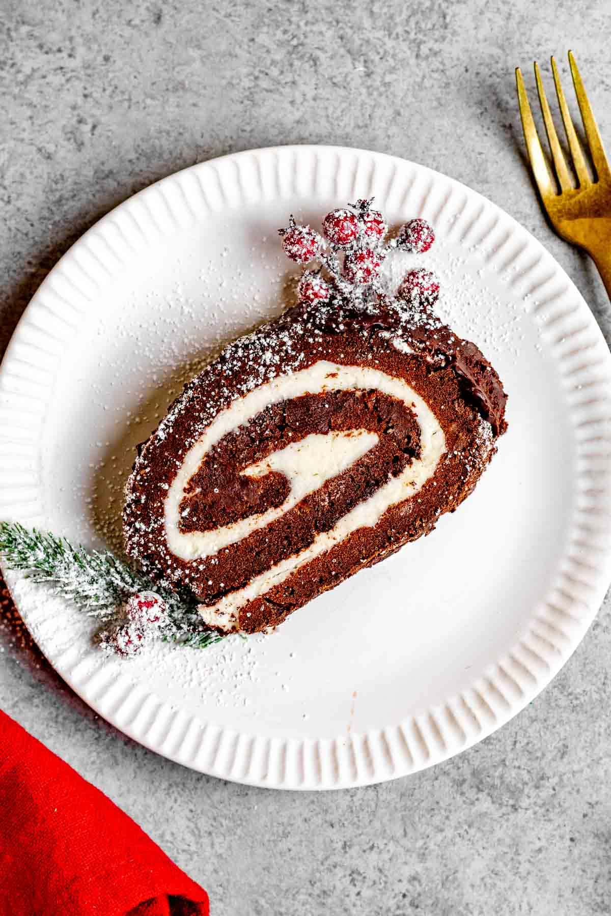 Chocolate Yule Log slice on plate with powdered sugar and holly garnish