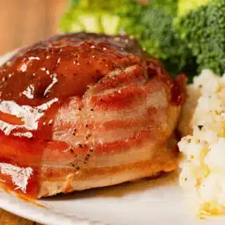 beef roll wrapped in a pork strip on a plate with broccoli and mashed potatoes