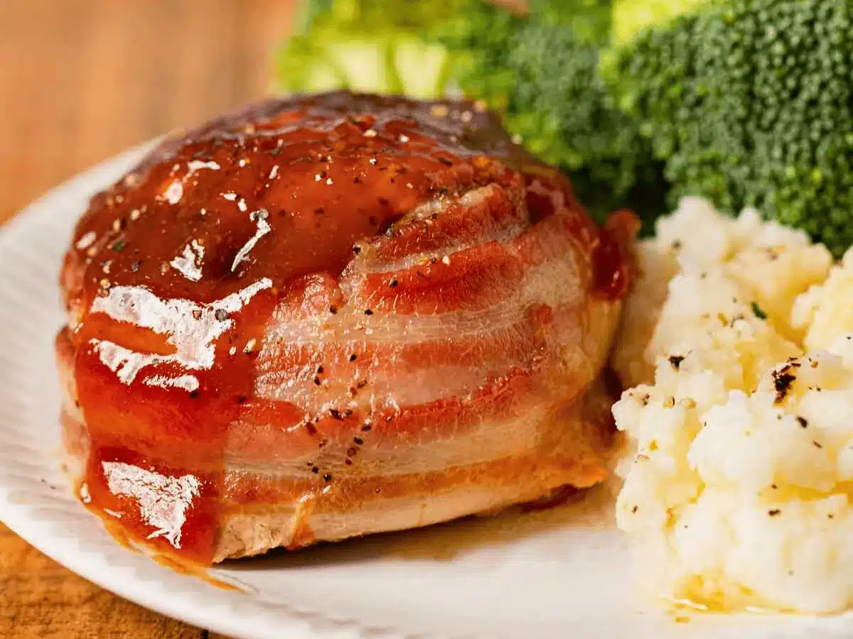 beef roll wrapped in a pork strip on a plate with broccoli and mashed potatoes