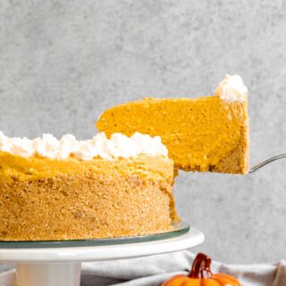 No-Bake Pumpkin Cheesecake being sliced from a white cake stand.