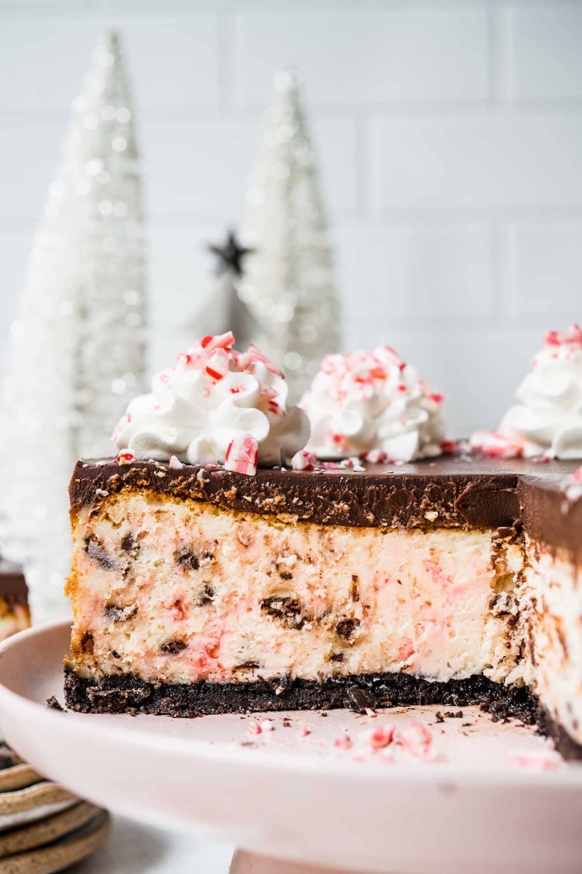 Peppermint Bark Cheesecake on cake plate with ganache topping, whipped cream and crushed candy canes on top