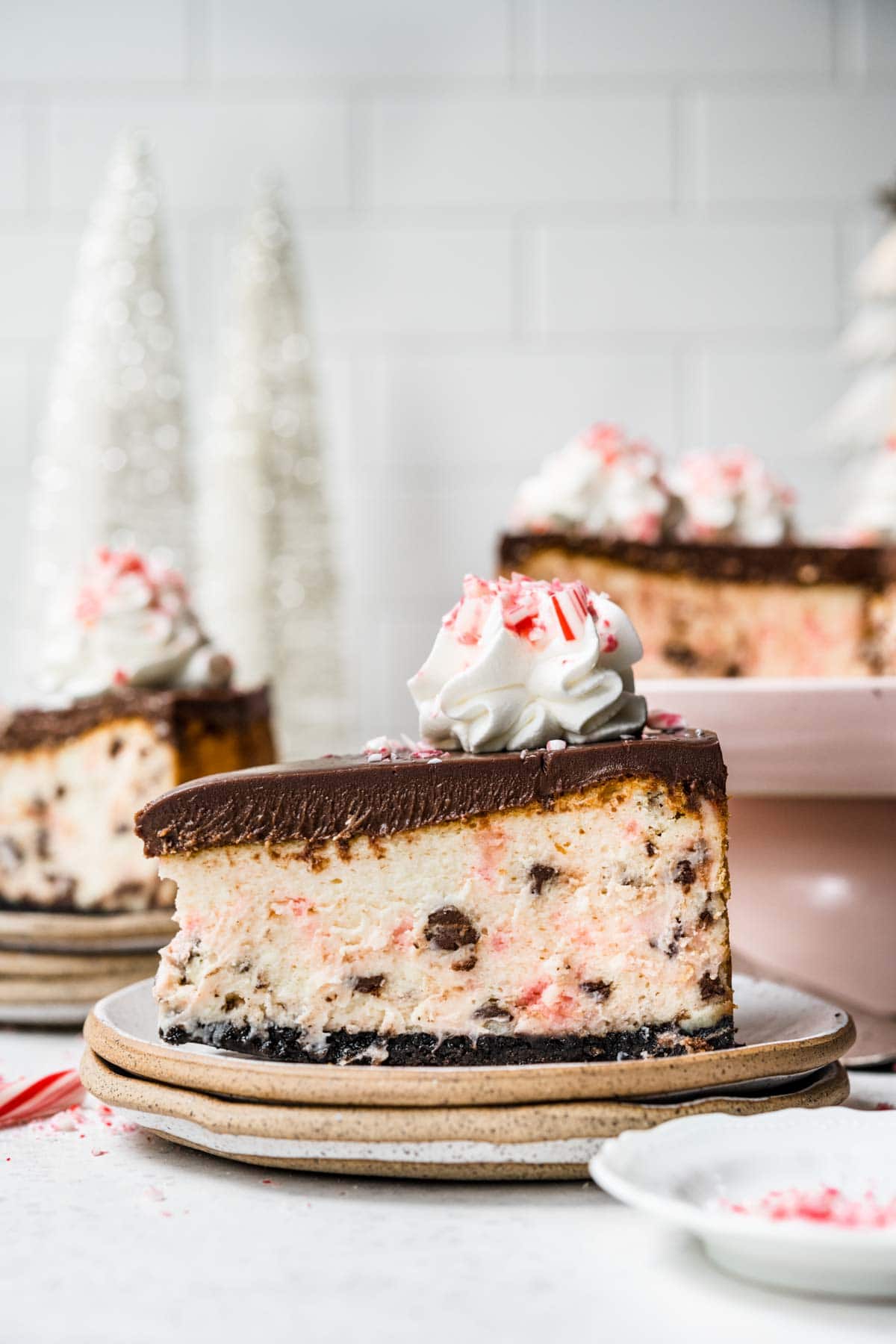 Peppermint Bark Cheesecake slice on plate with ganache topping, whipped cream and crushed candy canes on top