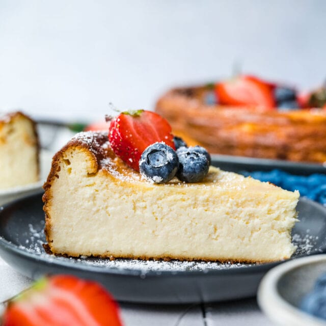 Ricotta Cheesecake slice on serving plate with fresh berries and powdered sugar on top