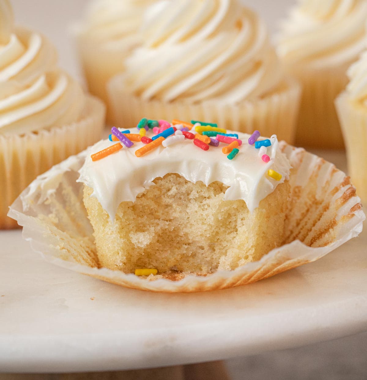 Vanilla Cupcakes with vanilla frosting and rainbow sprinkles with bite removed