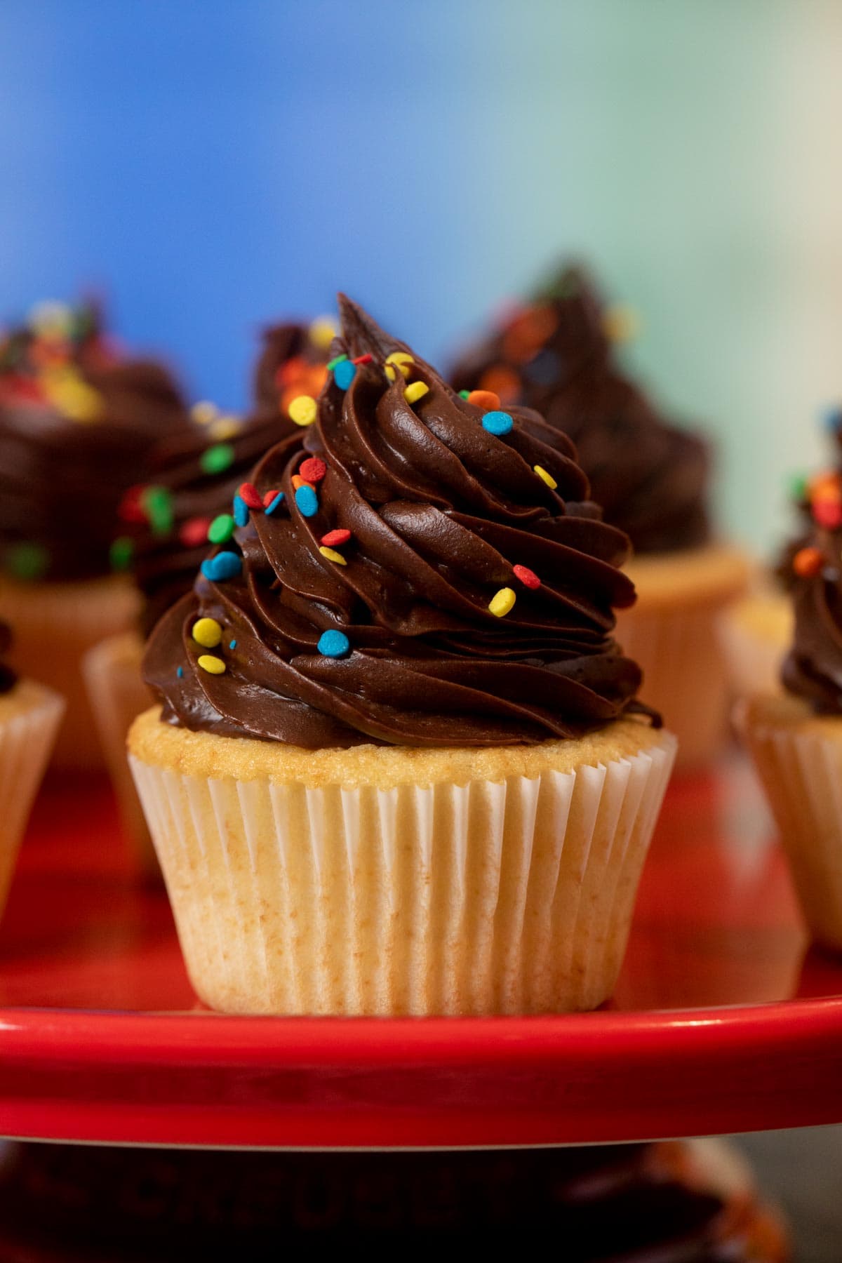 Yellow Cupcakes with Chocolate Frosting with rainbow sprinkles on cake stand