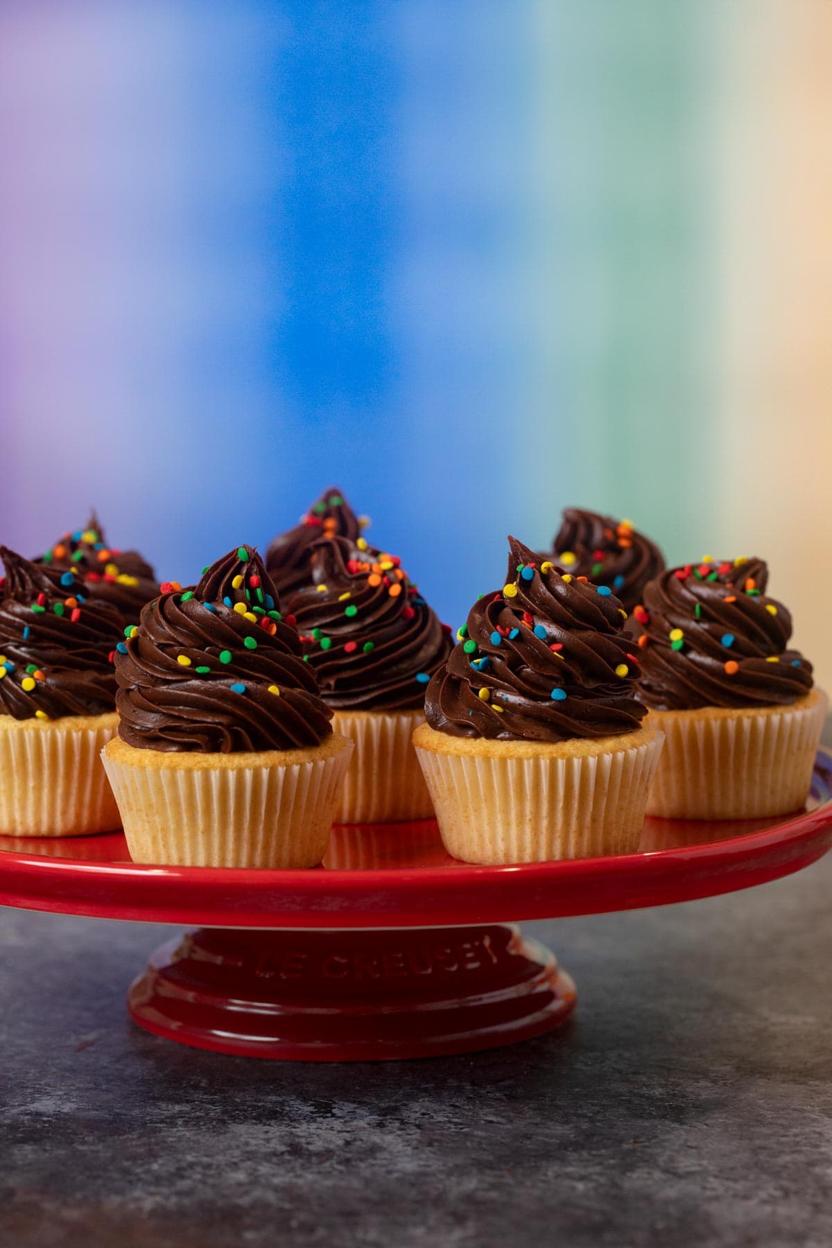 Yellow Cupcakes with Chocolate Frosting with rainbow sprinkles on cake stand