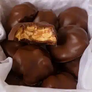 chocolates in a box with tissue paper and a bite taken out of one chocolate